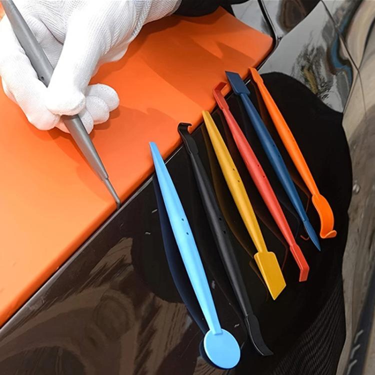 Car wrap tinting tools held in gloved hand; orange and blue edge squeegees