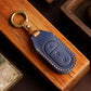 Blue genuine leather car key cover with brass keyring on wooden surface and stitched design