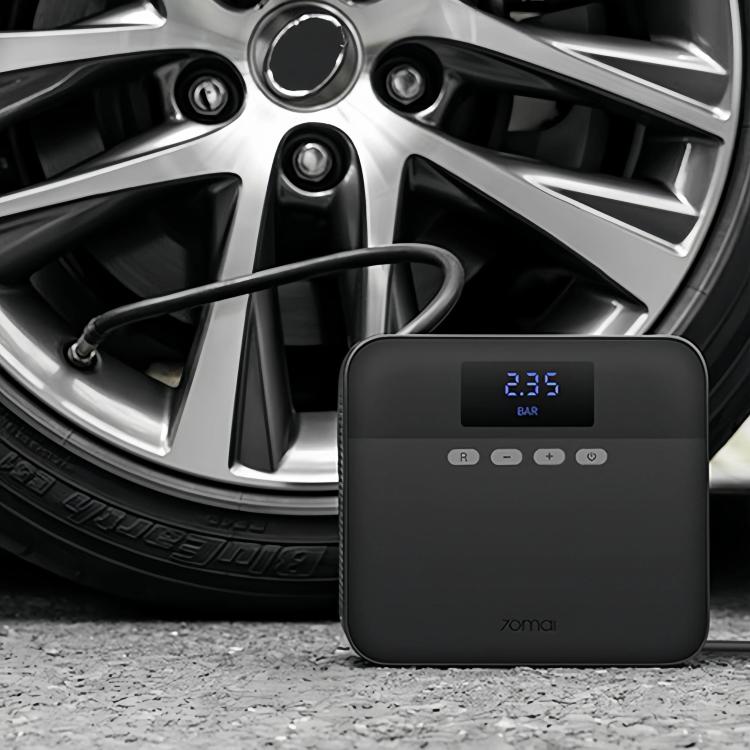 Black tire inflator resting near a car wheel, showing blue pressure readout