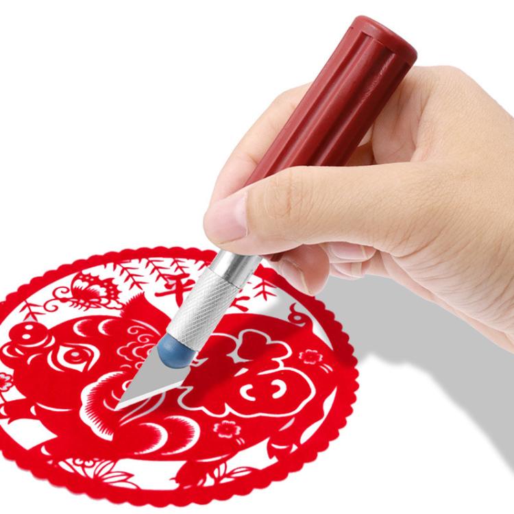 Hand using metal engraving cutter on red decorative paper disc