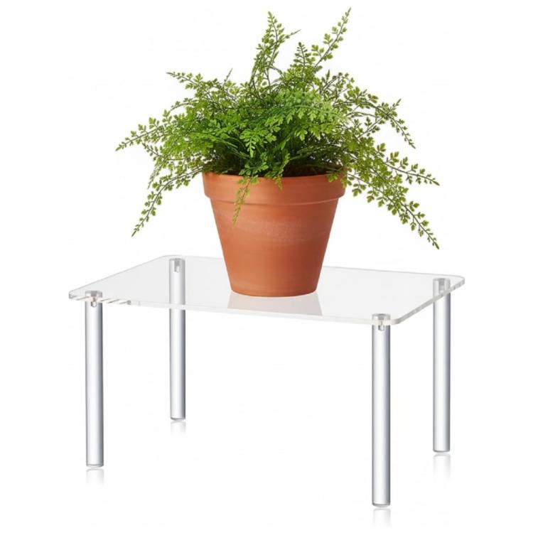 Clear acrylic plant stand with four chrome legs holding an orange terracotta pot