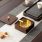 Square walnut wood ashtray with brass bowl, lid open, cigarette held near tray