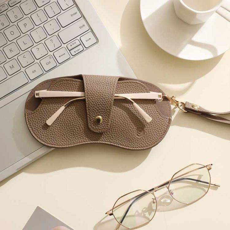 Brown PU leather hanging eyeglasses case with wrist strap on desk next to glasses