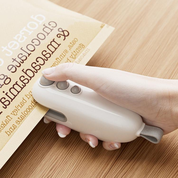 White mini bag sealer held in hand, pressing onto an open food bag for sealing.