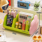 Green and pink cosmetic storage rack with open front holds markers, a book, and a phone