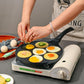 Nonstick 7-cup egg burger pan with fried eggs in wells on a small tabletop griddle.