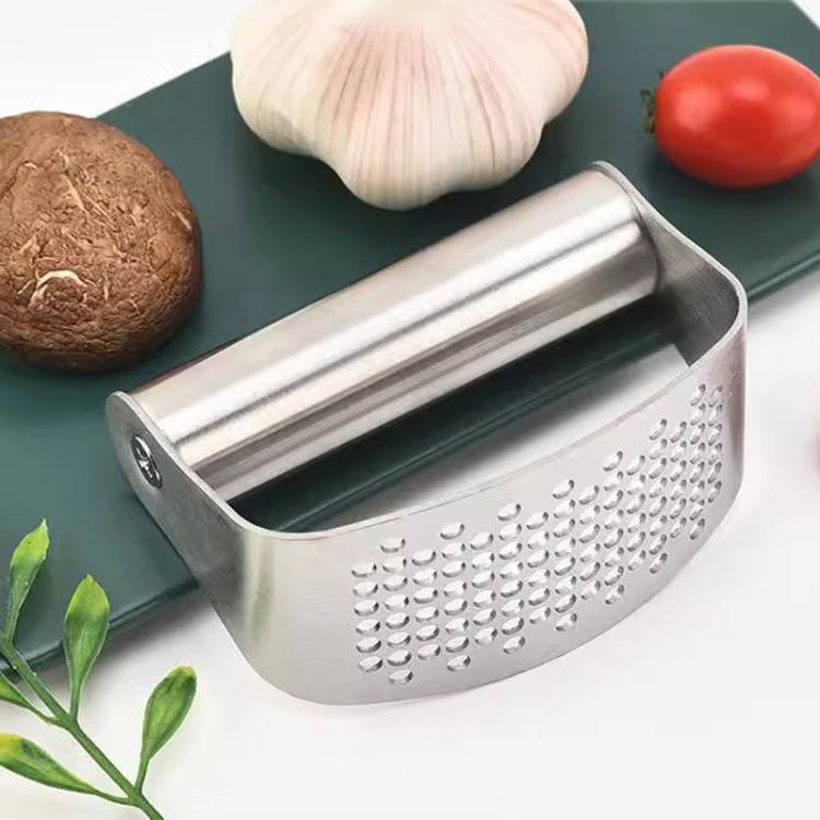 Stainless steel curved garlic press with perforated panel, garlic cloves nearby