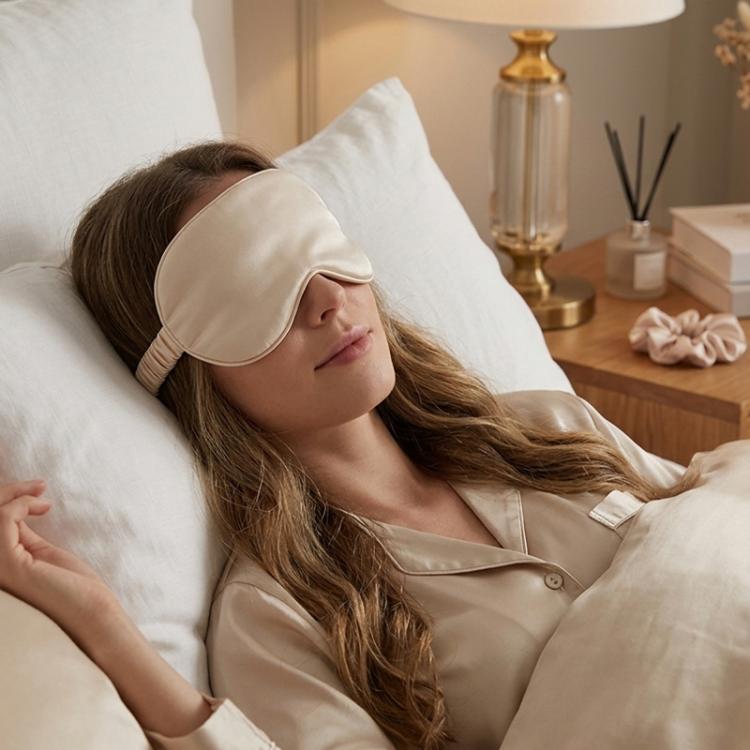 Cream satin sleep mask worn on a person lying down for eye coverage.