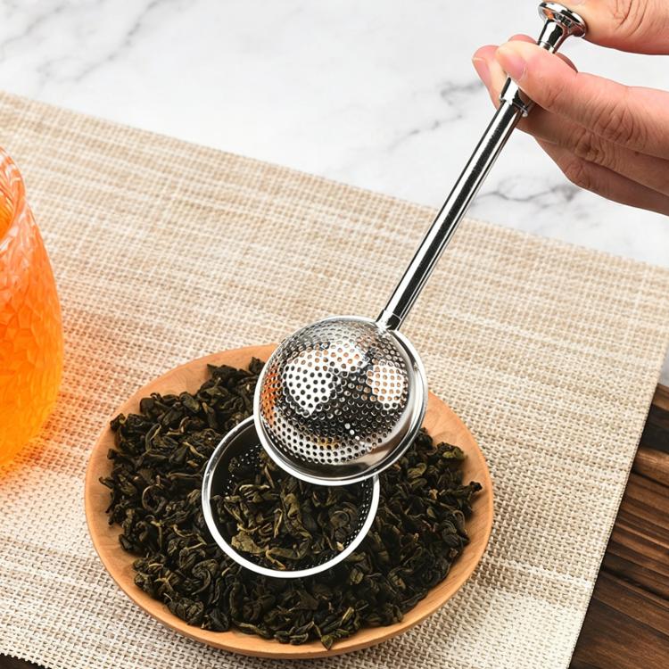Stainless steel round tea infuser mesh with handle, held over tea leaves in a bowl