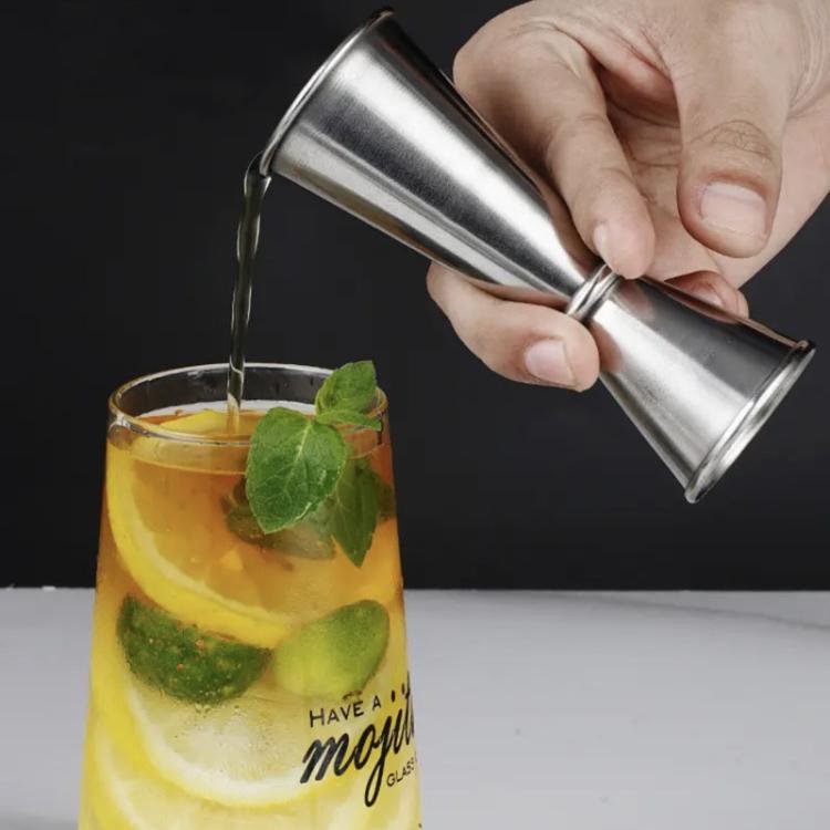 Stainless steel jigger pour cup tilted over drink