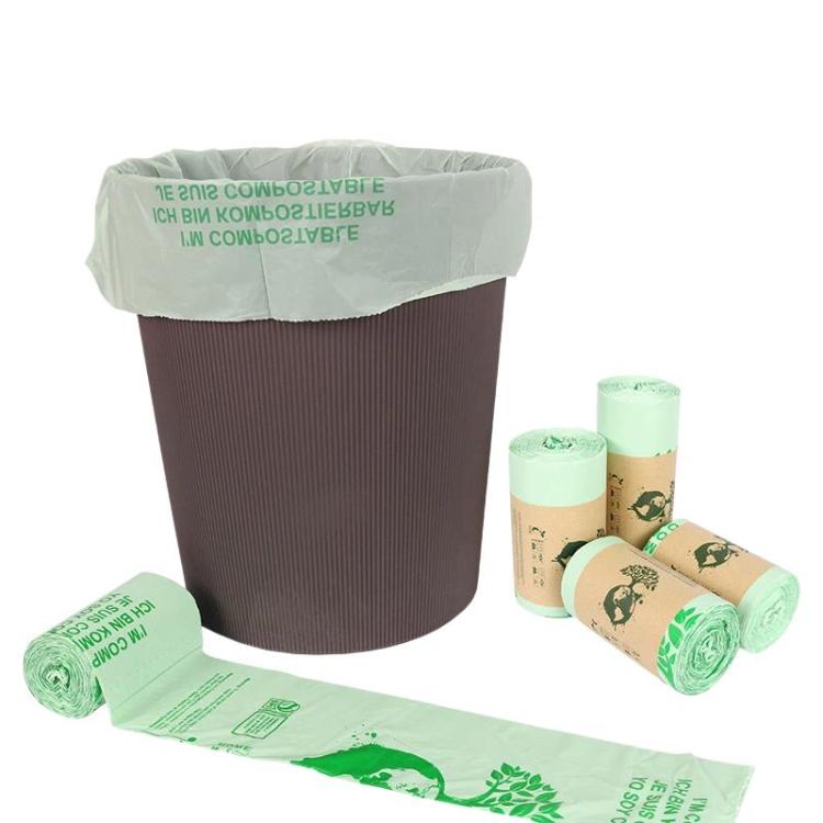 Compostable PLA garbage bag liner on a bin with rolled bags, light green and brown