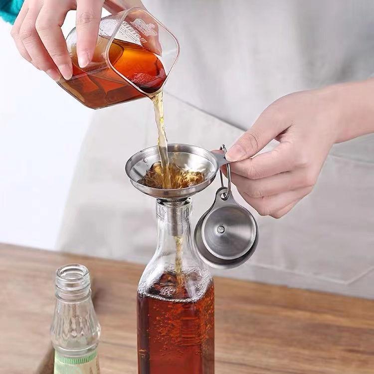 Stainless steel funnel liquid dispenser pouring from bottle into a measuring cup