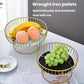 Two round wrought iron fruit trays with gold frames, holding bananas, peaches, and grapes.