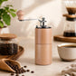 Light wood hand-cranked coffee grinder standing on counter with metal grinding mechanism