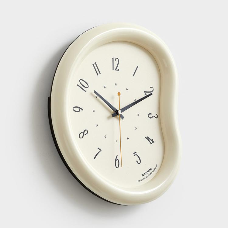 Cream wall clock with light face, minimalist hands and number markers, curved frame