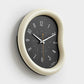 Cream framed wall clock with dark face, minimalist hands and number markers, oval case