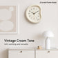 Cream curved-frame wall clock with black numbers and gold-tipped hands