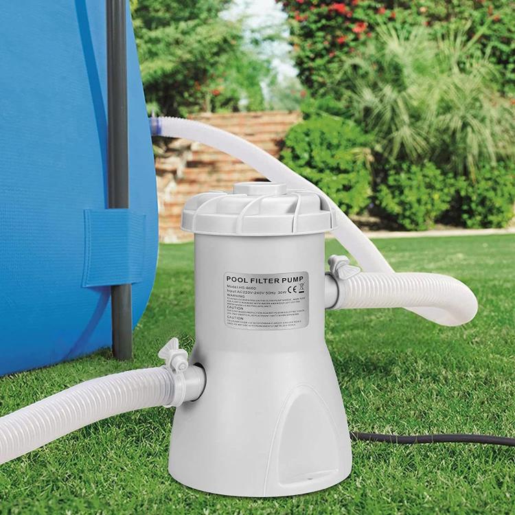 White pool filter pump standing on grass with two hose connections and outlet spout