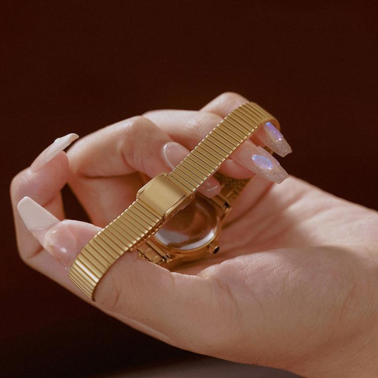 Gold-tone ribbed expansion watch band with small round case, shown in hand