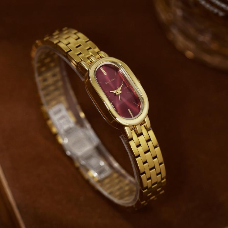 Gold oval quartz dress watch with maroon dial on a gold metal bracelet