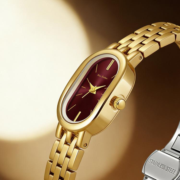 Close-up of gold oval quartz dress watch with maroon dial and gold crown