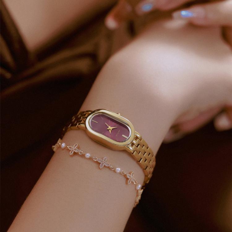 Gold metal oval quartz dress watch with maroon dial on a wrist