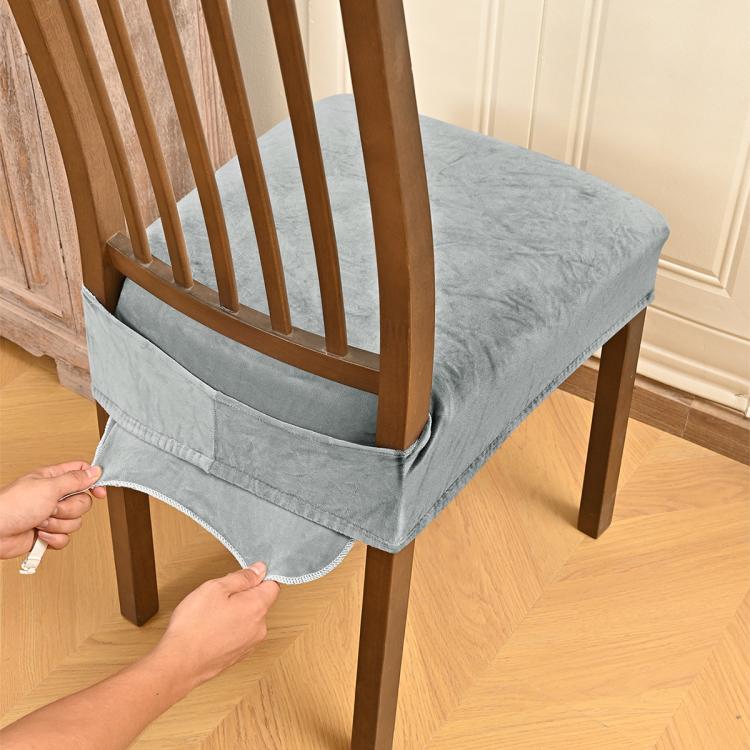 Gray velvet stretch chair seat cover with buckle straps, being fitted on dining chair