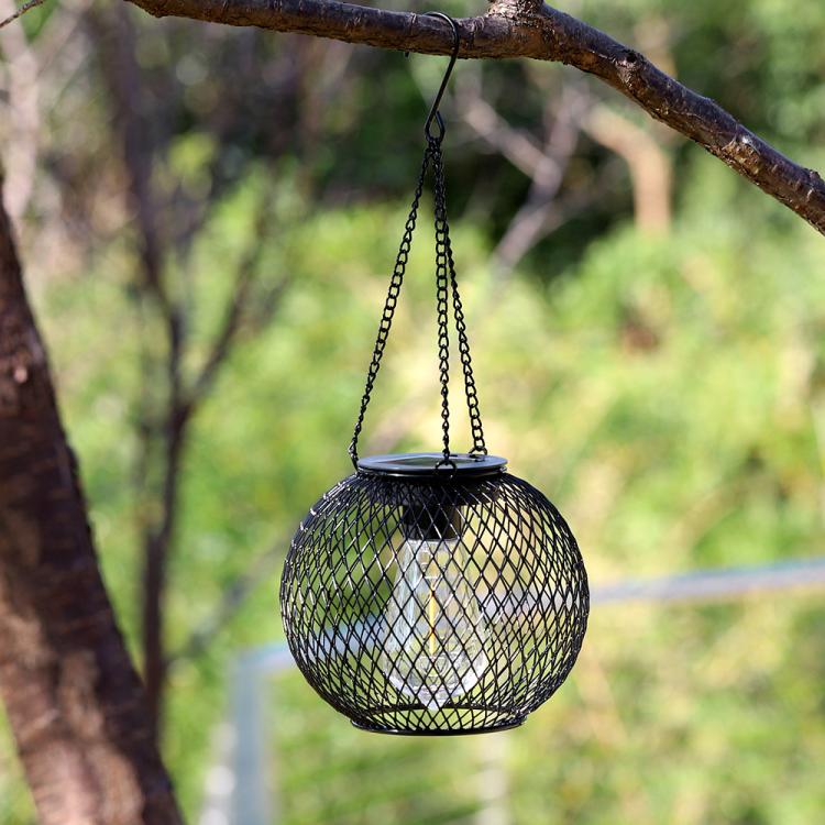 Outdoor hanging black metal mesh globe lantern under a tree branch