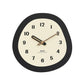 Minimalist oval wall clock close-up with cream dial, dark rim, and gold hands