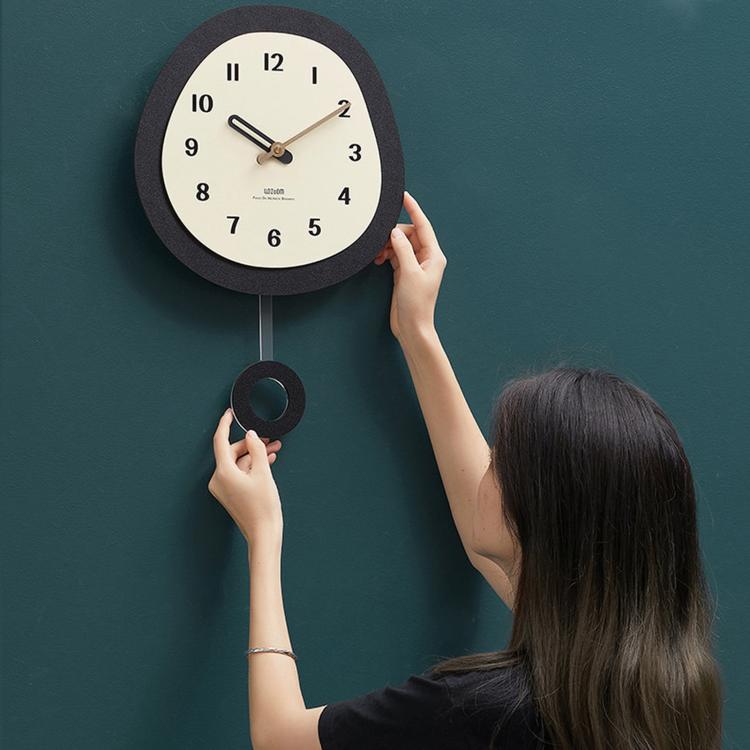 Oval wall clock being installed, dark frame and cream dial with walnut wood hands