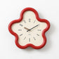 Flower-shaped wall clock with red frame, cream face, black hands and Arabic numerals.