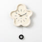 Flower-shaped wall clock with cream frame, cream face, black hands; hanging cord visible.