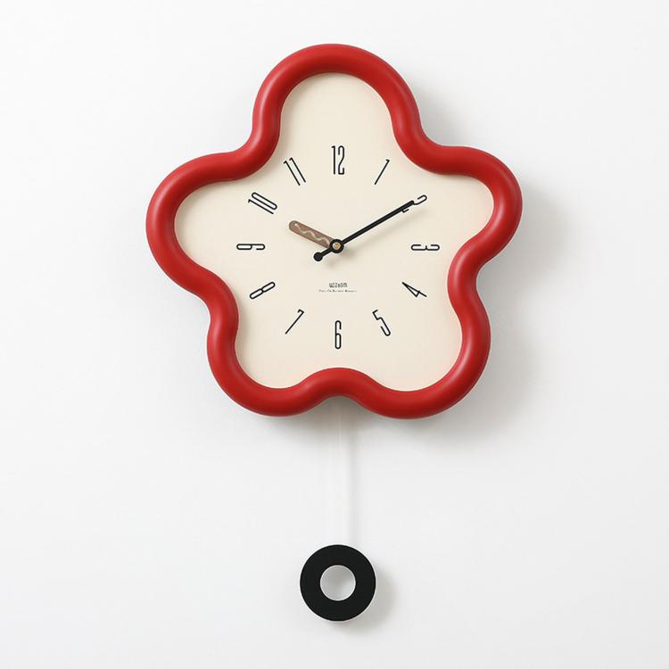 Flower-shaped wall clock with red frame, cream face, black hands; hanging cord visible.