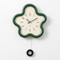Flower-shaped wall clock with green frame, cream face, black hands and Arabic numerals.