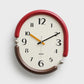 Retro oval wall clock with red frame, cream dial, brown and black hands.