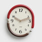 Retro oval wall clock with red frame, cream dial, striped gold hands and black hour marks.
