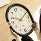 Retro oval wall clock with black frame, cream dial, gold and black hands, wood accents.