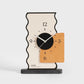 Geometric desk clock with cream back, black dial, orange panel, and slender line hands