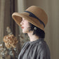 Straw cloche sun hat with dark band and ribbon bow, worn by a woman profile