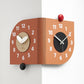 Orange dual-dial corner wall clock with white hands and red and black knobs