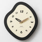 Irregular wall clock with black frame, cream face, and gold-toned clock hands.