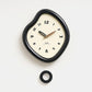Irregular wall clock with glossy dark frame and cream dial, plus mounting ring piece.