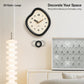 Large irregular wall clock with glossy black frame, cream dial, and gold-toned hands.