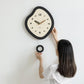 Irregular black wall clock with cream dial, walnut hands, and round mounting ring