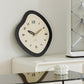 Irregular wall clock with black frame, cream dial, walnut hands, and Arabic numerals