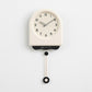Cream pendulum wall clock with off-white dial, black hands, and hanging pendulum weight.