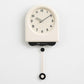 Cream pendulum wall clock with light dial, black hands, and hanging pendulum weight.