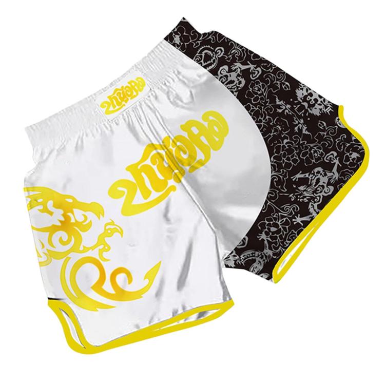 White and black Muay Thai shorts with gold pattern, curved side panel, and elastic waist