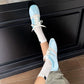 Light blue lace-up sneakers with white laces and white soles, worn with rolled socks