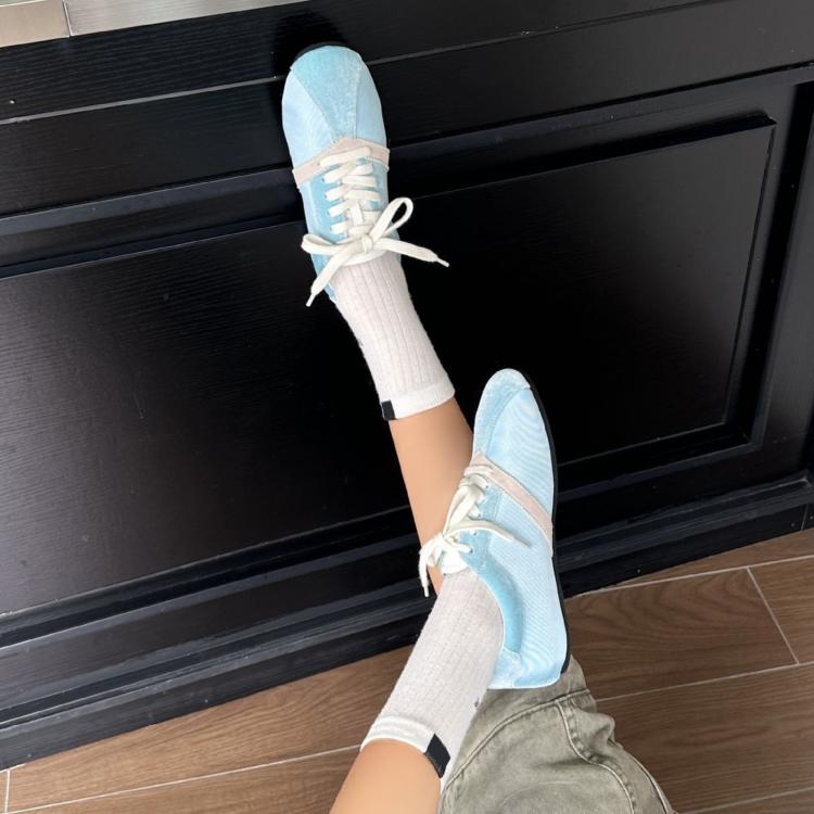 Light blue lace-up sneakers with white laces and white soles, worn with rolled socks